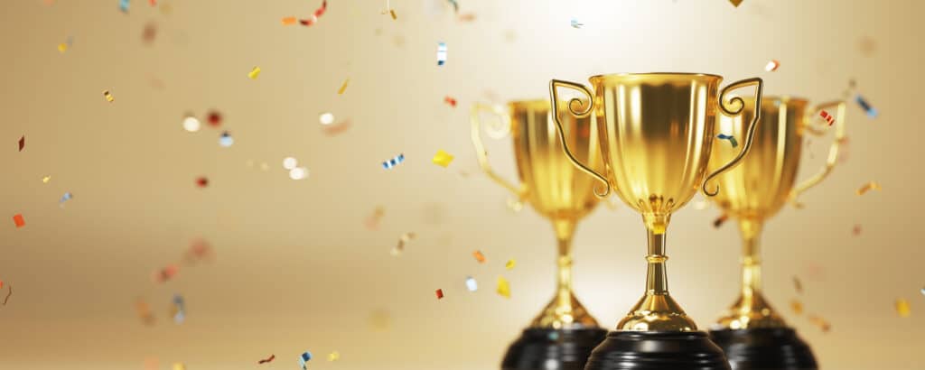 An image of three gold coloured trophies with confetti falling around them on a yellow background